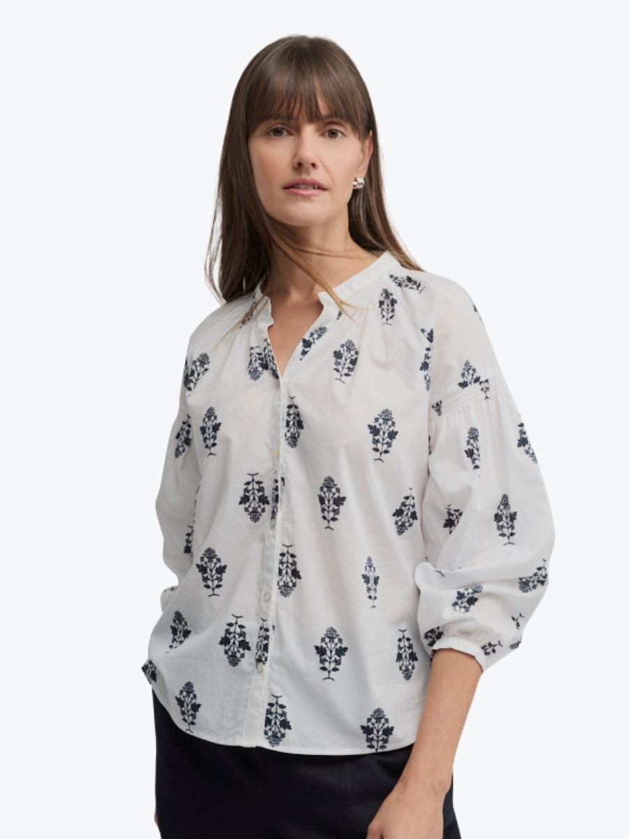 Woman wearing a white blouse with black floral patterns on a white background