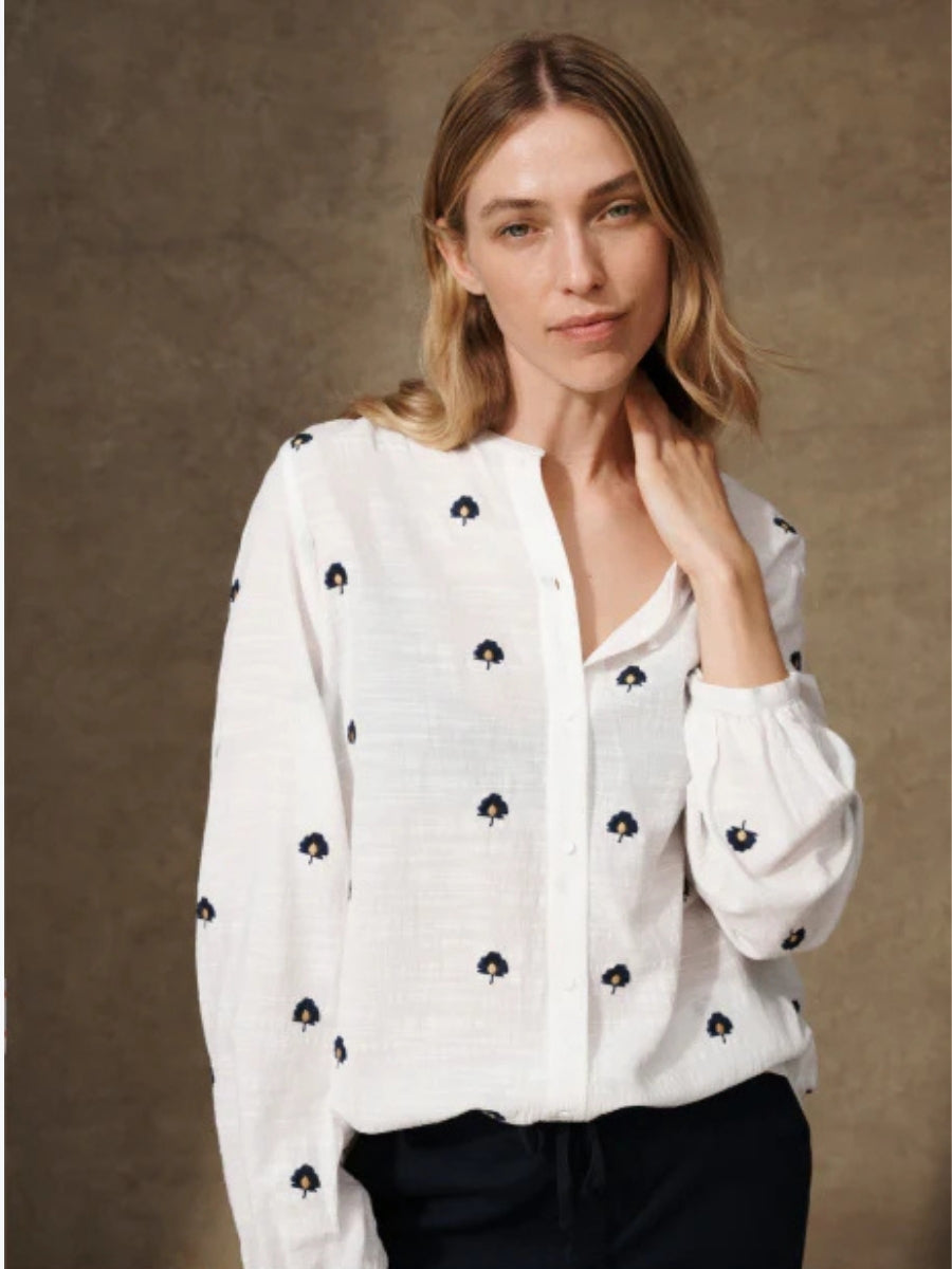 Woman wearing a white blouse with black floral patterns against a brown background