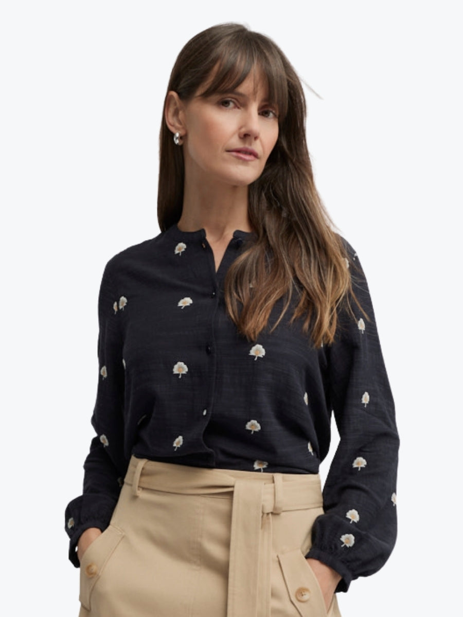 Woman wearing a black blouse with white patterns and beige pants on a white background