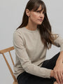 Woman wearing a beige sweater sitting on a wooden chair against a plain background